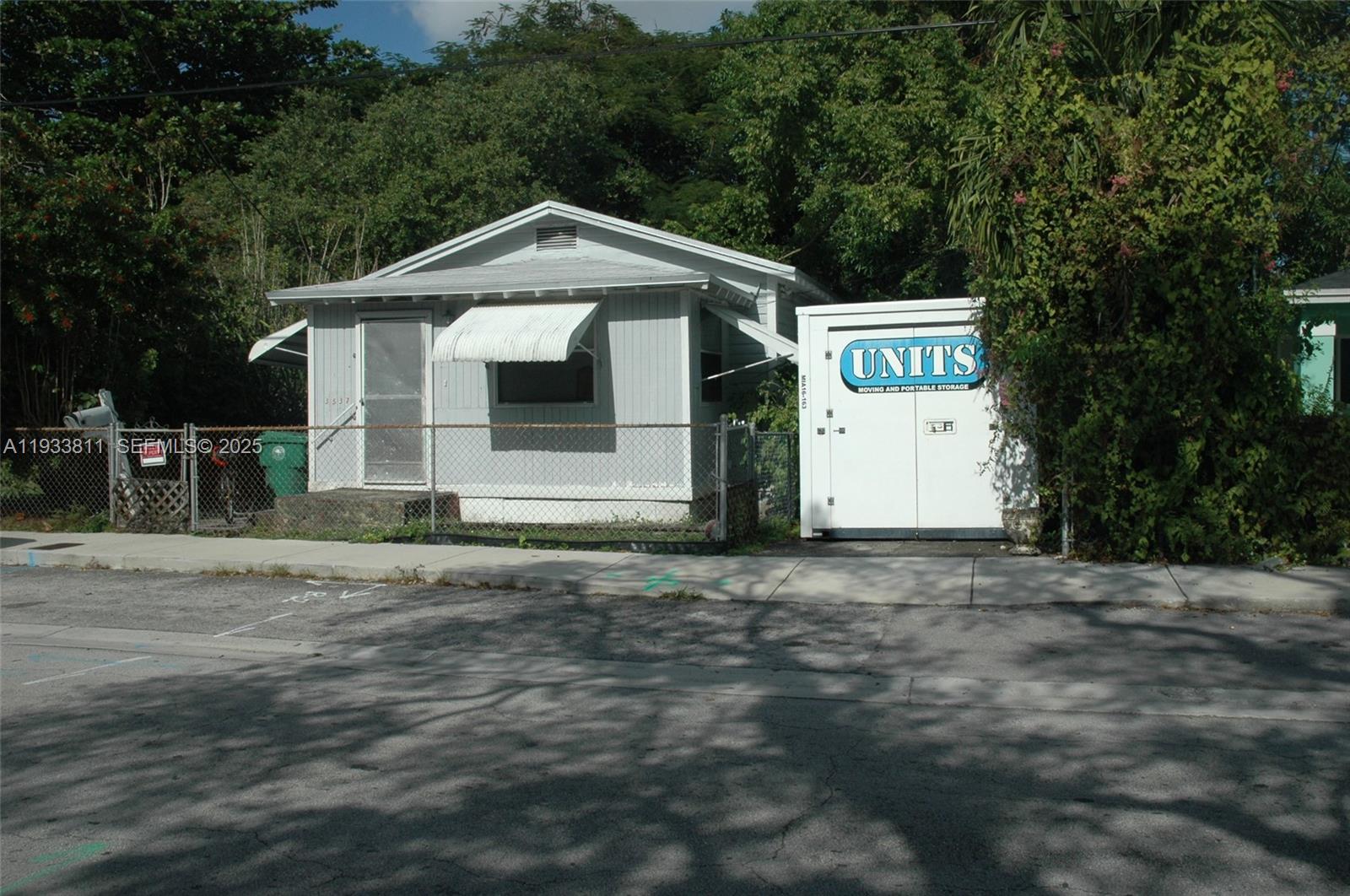 A small, light-gray house with a metal awning sits behind a chain-link fence — 3537 Charles Ave, Miami FL 33133, MIAMI, FL