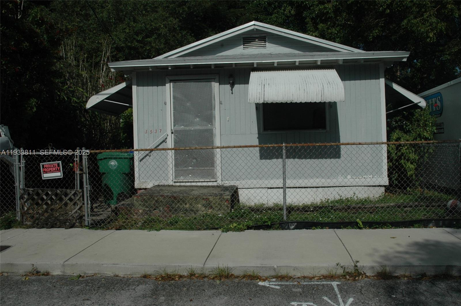 A small, light-gray, single-story house with a metal awning and a chain-link fence — 3537 Charles Ave, Miami FL 33133, MIAMI, FL