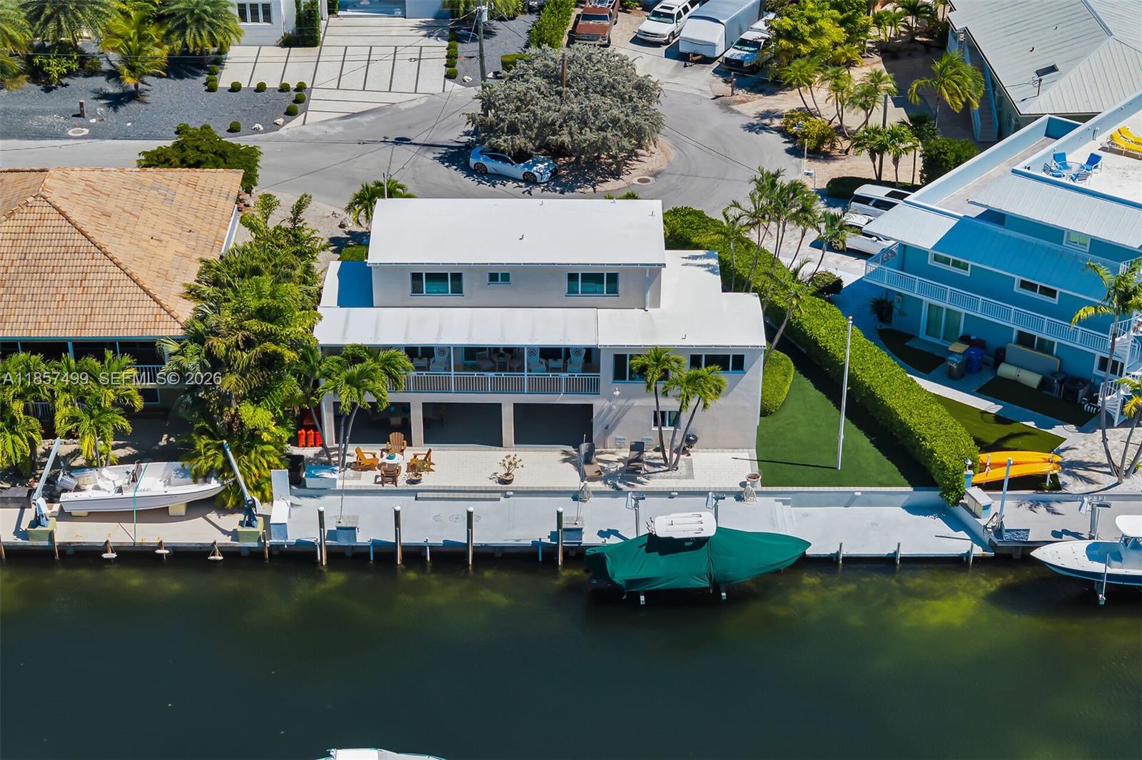 A three-story waterfront house features a boat lift, a concrete dock, and a grassy yard — 122 Court Contessa, Islamorada FL 33036, ISLAMORADA, FL