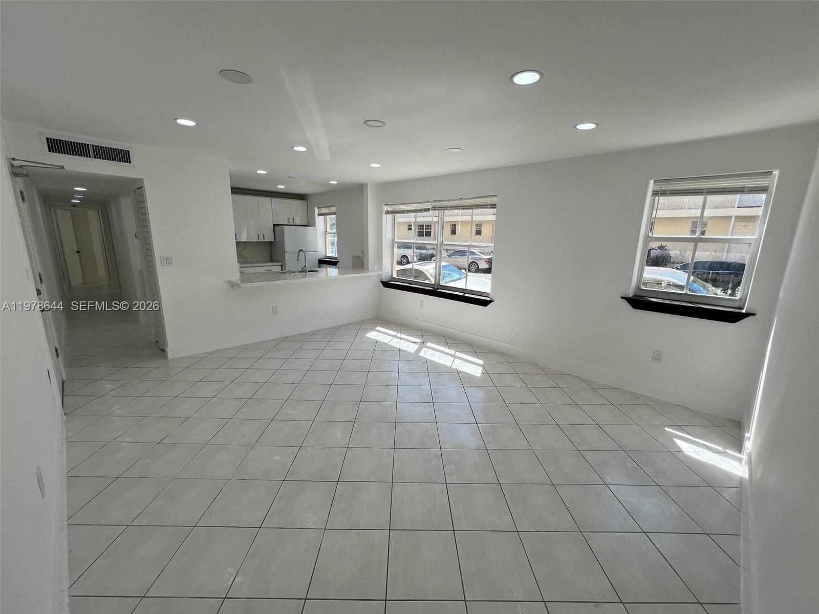 A bright, open-concept living area features white tile flooring, recessed lighting, and a kitchen pass-through — 1308 Drexel Ave # 103, Miami Beach FL 33139, MIAMI BEACH, FL