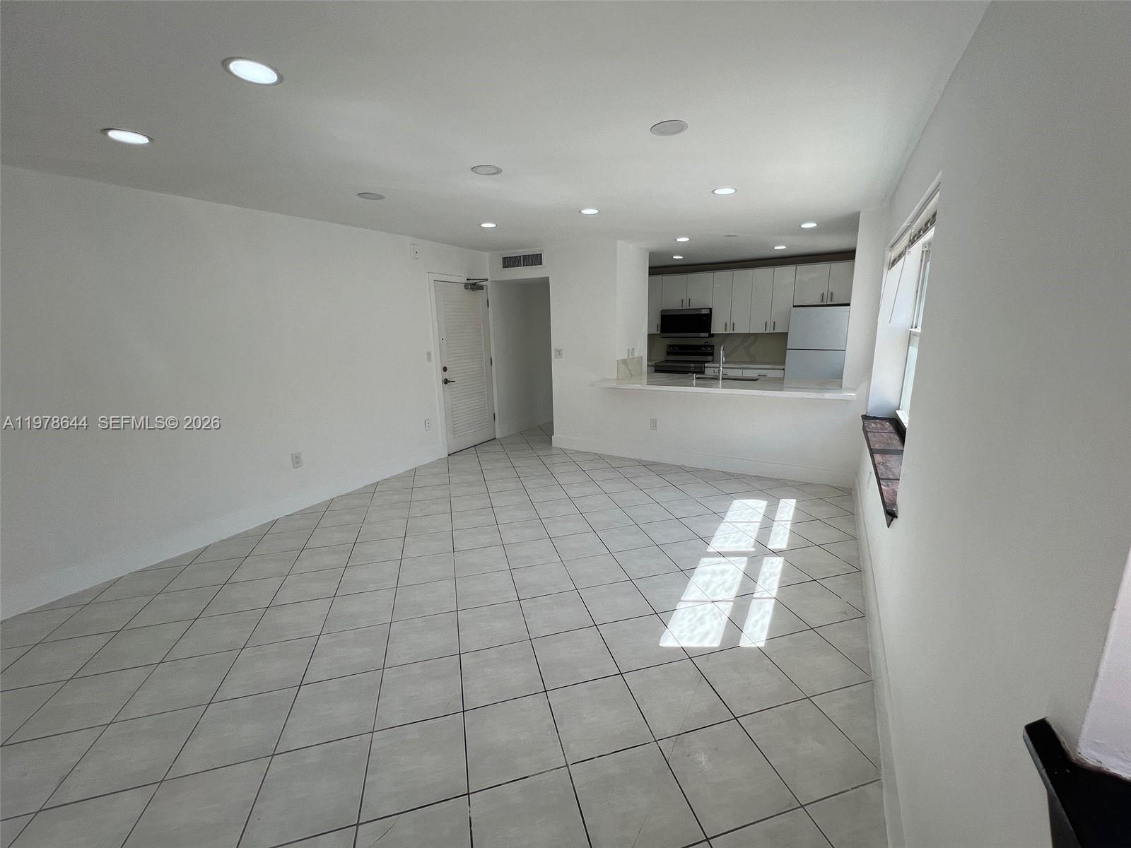 An open-concept living area features white walls, tile flooring, and an adjacent kitchen — 1308 Drexel Ave # 103, Miami Beach FL 33139, MIAMI BEACH, FL