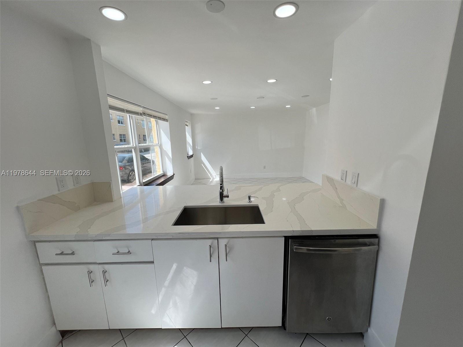 A kitchen features white cabinets, a quartz countertop with a sink, and a stainless dishwasher — 1308 Drexel Ave # 103, Miami Beach FL 33139, MIAMI BEACH, FL
