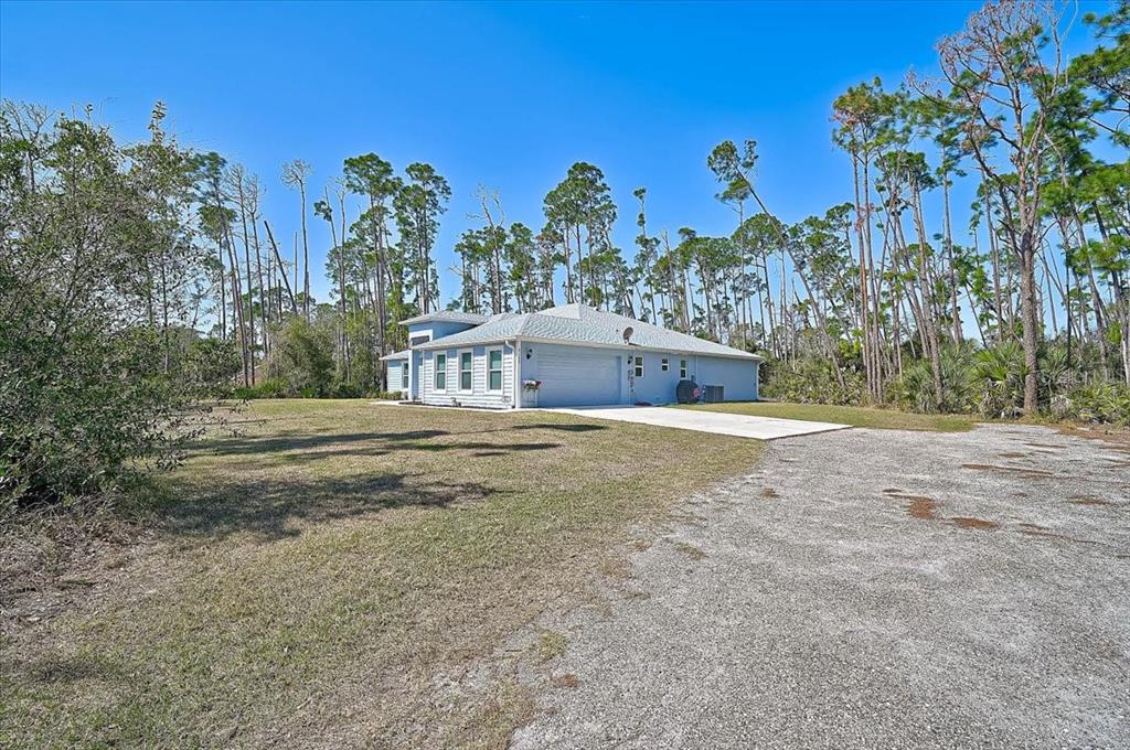 A light blue single-story house with a gravel driveway sits among tall pine trees — 4109 N CRANBERRY BOULEVARD, NORTH PORT, FL