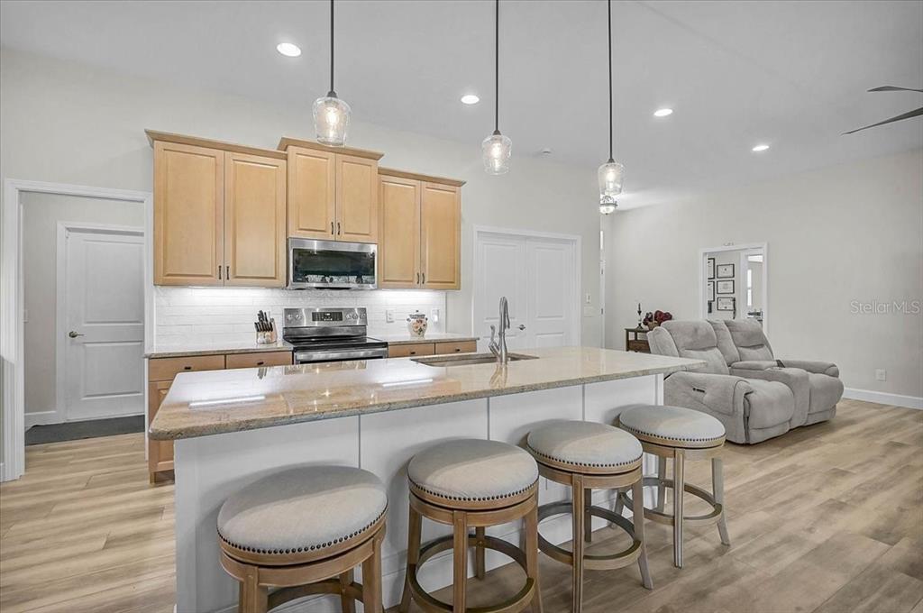 A kitchen features light wood cabinets, a granite island with bar stools, and pendant lighting — 4109 N CRANBERRY BOULEVARD, NORTH PORT, FL
