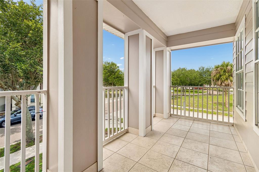 A covered balcony with light-colored tile flooring and white railings overlooks a grassy area — 3801 MACHADO STREET, TAMPA, FL