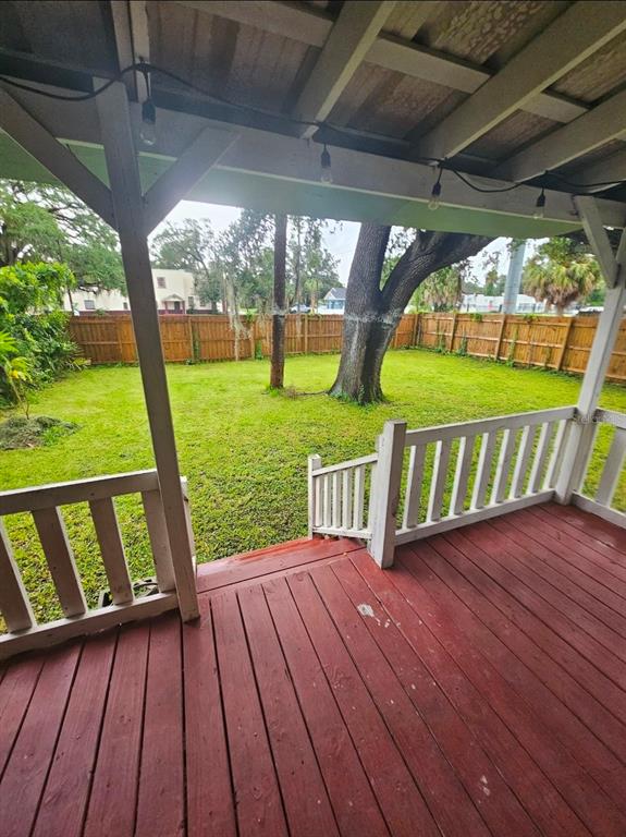 A red wooden deck overlooks a grassy backyard enclosed by a wooden privacy fence — 2634 E 26TH AVENUE, TAMPA, FL