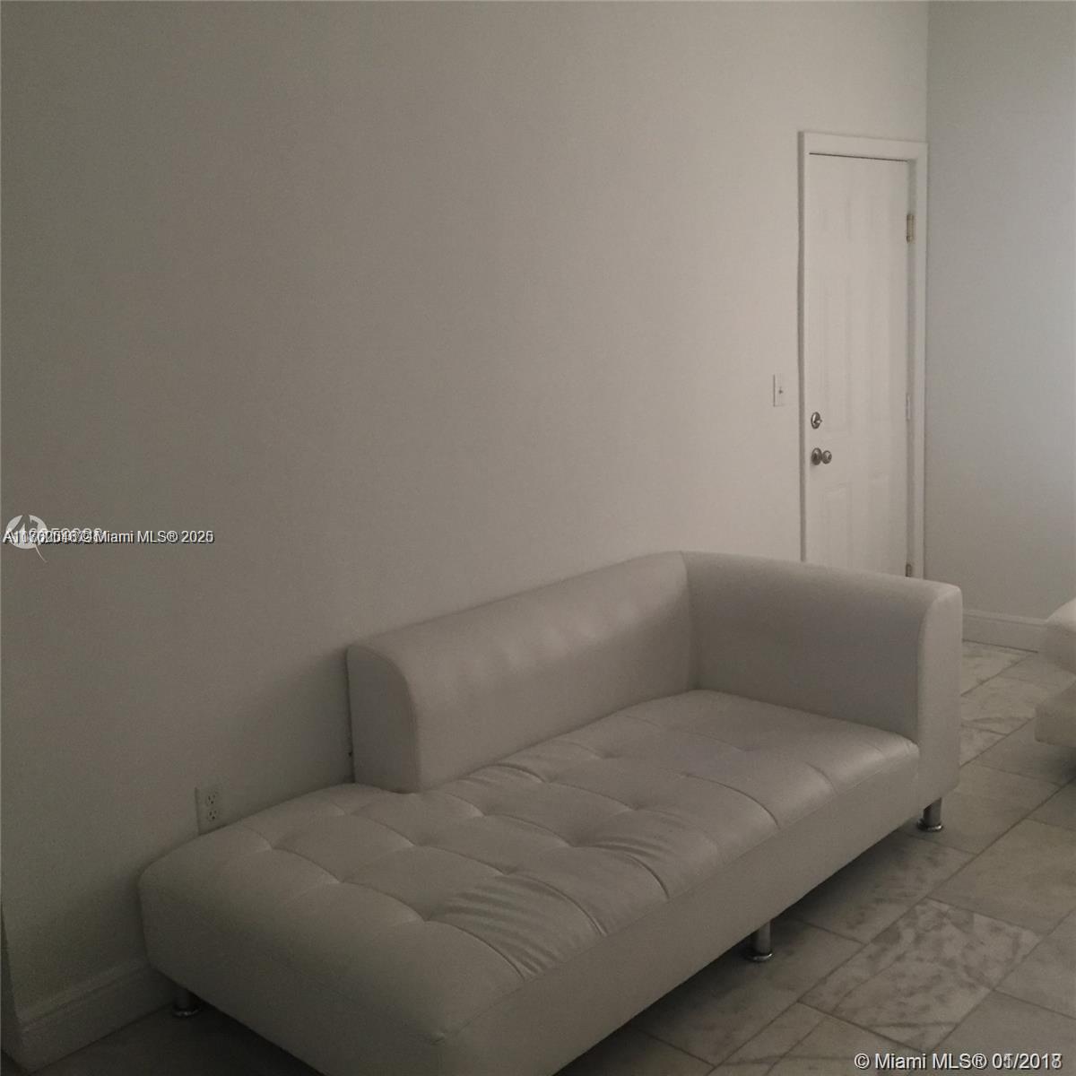 A white tufted sofa sits against a plain wall near a closed white door — 918 Jefferson Ave # 2, Miami Beach FL 33139, MIAMI BEACH, FL