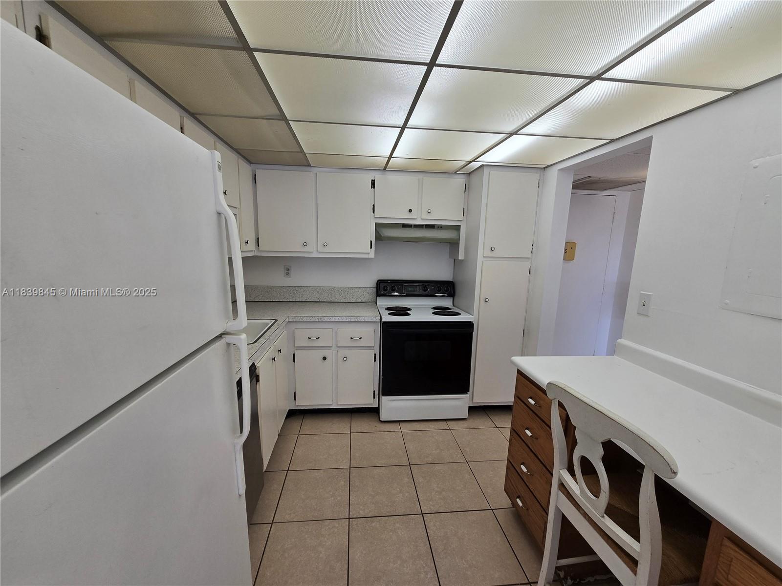 A kitchen features white cabinetry, a white stove, a refrigerator, and a drop ceiling — 2731 Taft St # 102, Hollywood FL 33020, HOLLYWOOD, FL