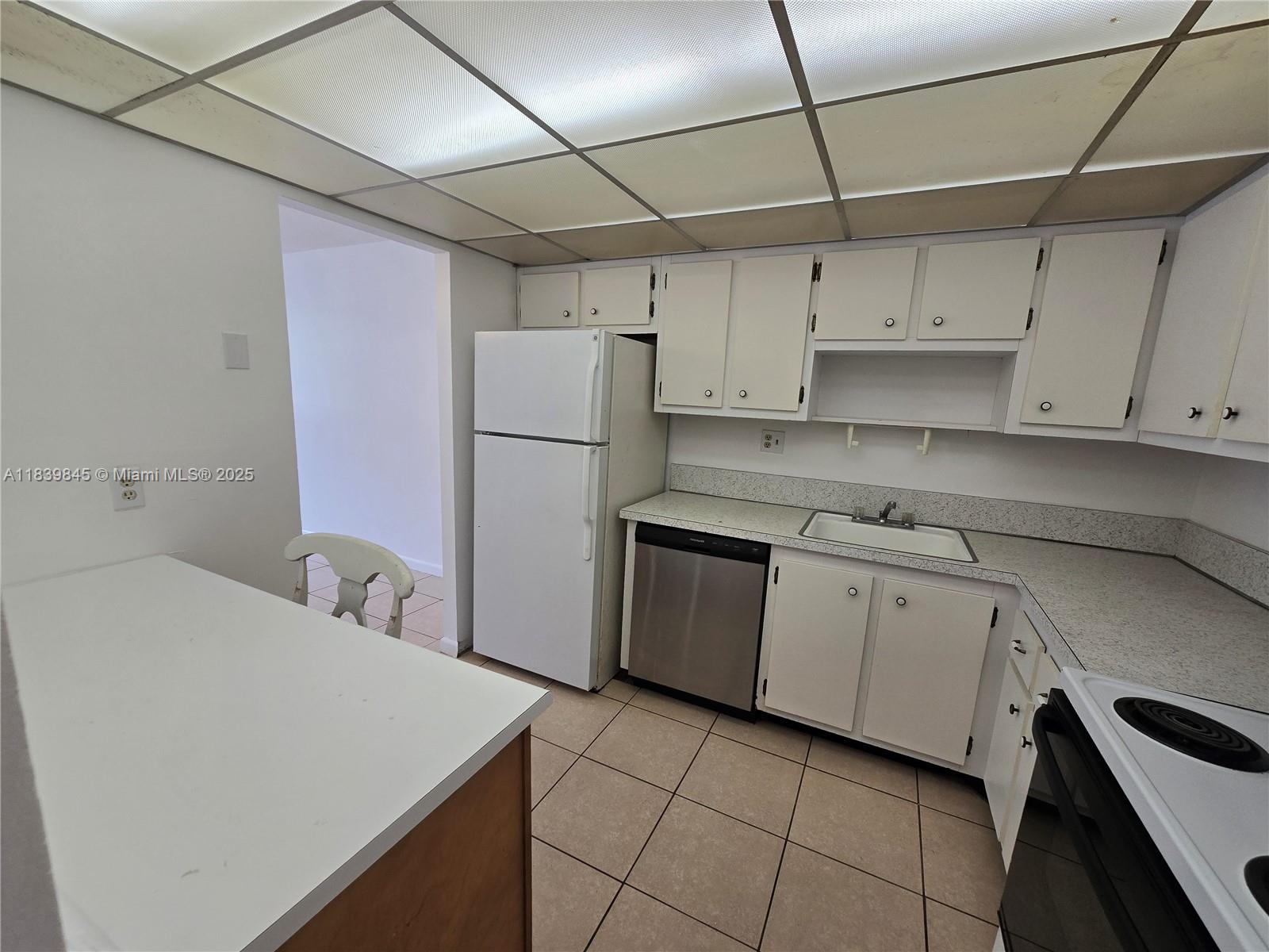 A kitchen features white cabinetry, a stainless steel dishwasher, a white refrigerator, and tiled flooring — 2731 Taft St # 102, Hollywood FL 33020, HOLLYWOOD, FL