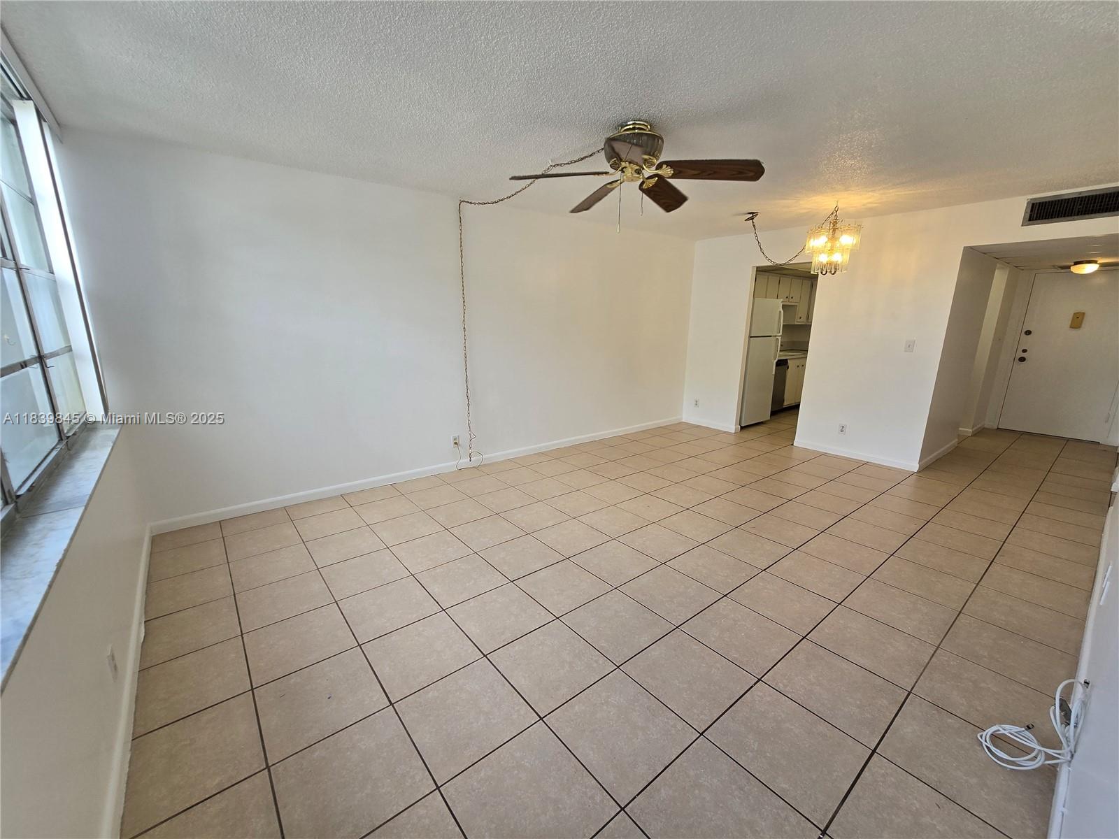 An empty living room features beige tile flooring, a ceiling fan, and an adjacent kitchen — 2731 Taft St # 102, Hollywood FL 33020, HOLLYWOOD, FL