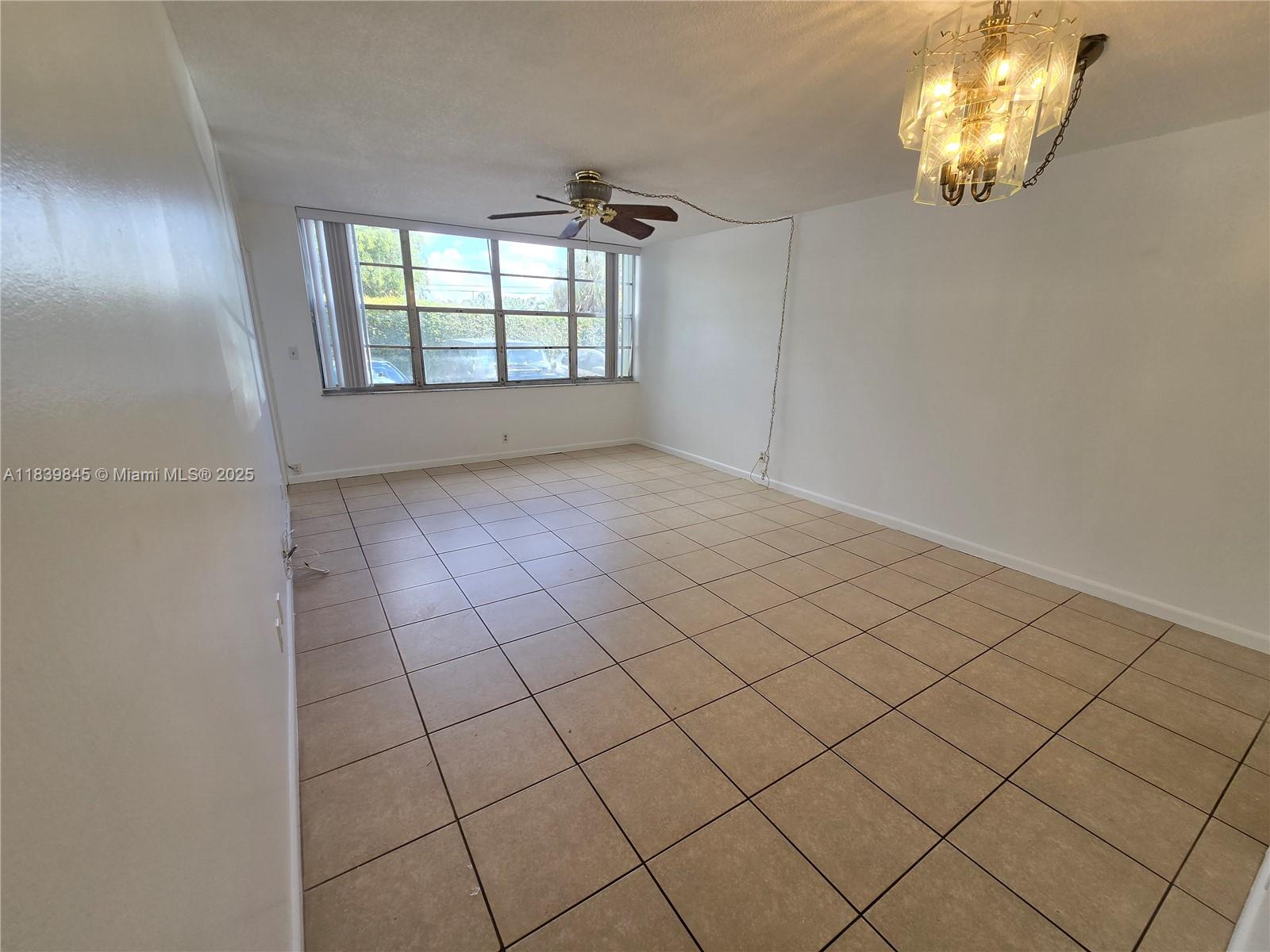 An empty room features beige tile flooring, a ceiling fan, and a hanging light fixture — 2731 Taft St # 102, Hollywood FL 33020, HOLLYWOOD, FL