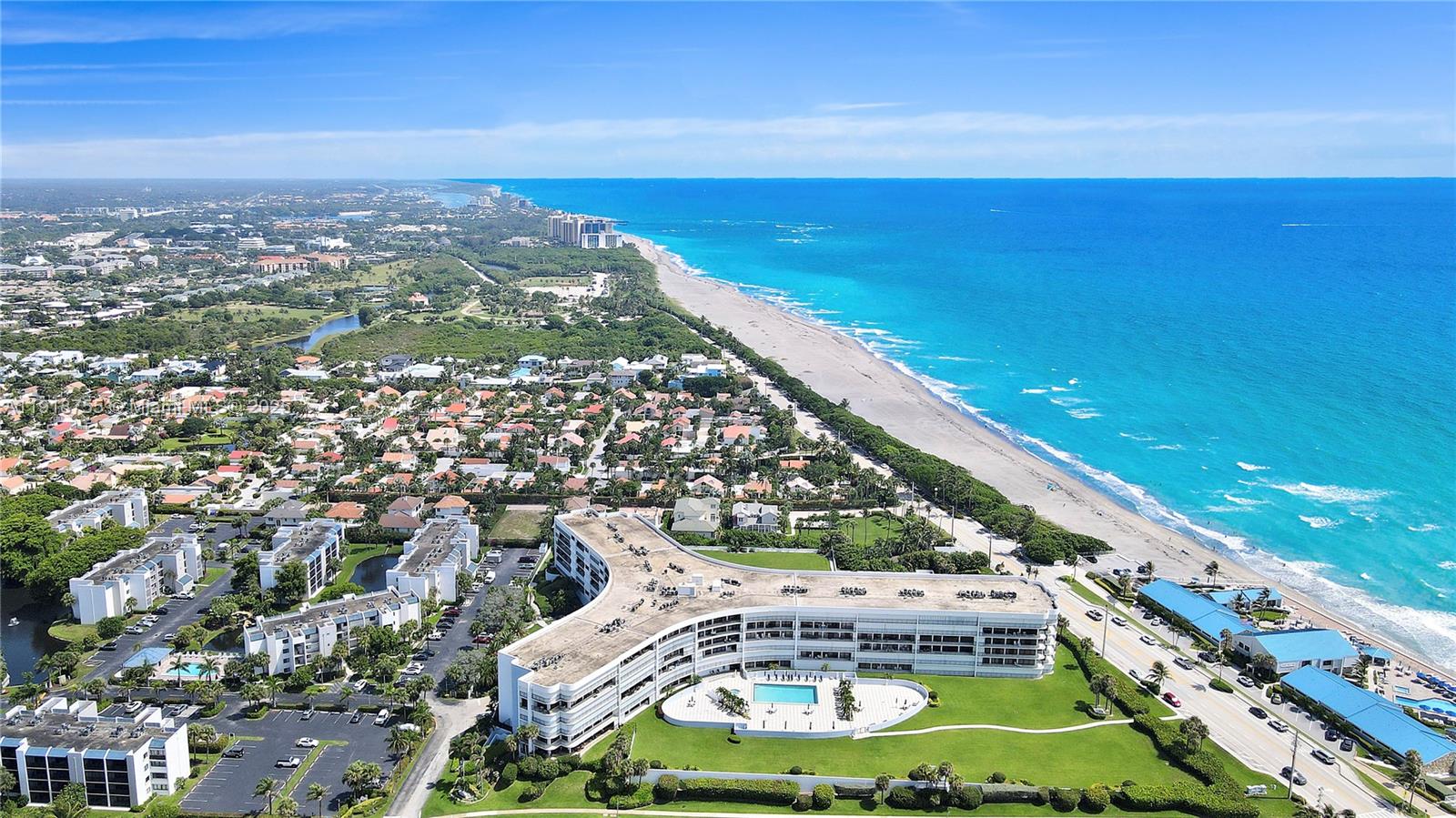 An aerial view shows a large, curved beachfront condominium complex with a pool and parking — 1300 S Highway A1a # 227, Jupiter FL 33477, JUPITER, FL