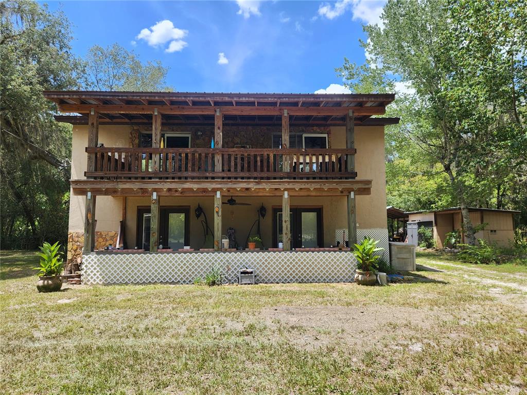 A two-story house with a wooden balcony and a covered ground-level patio with lattice skirting — 13501 NE 245TH STREET ROAD, FORT MC COY, FL