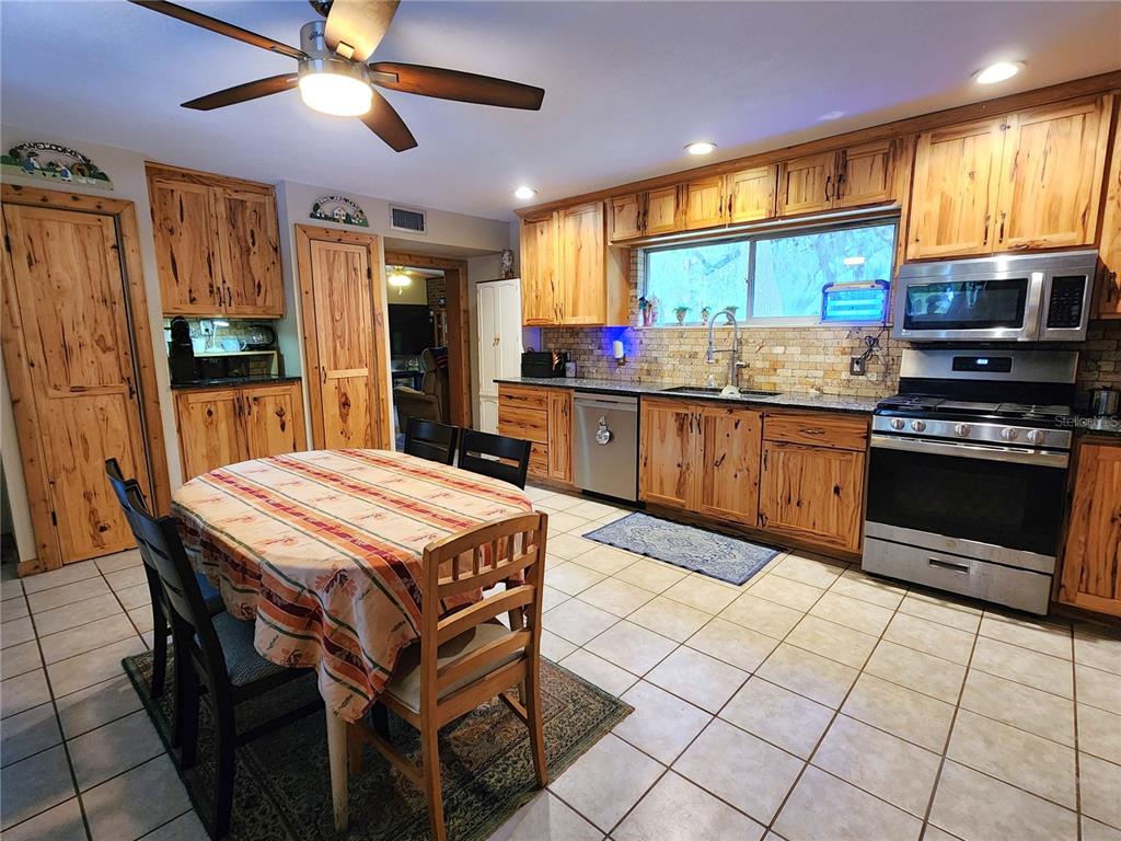 A kitchen features knotty wood cabinets, stainless steel appliances, and a dining table with chairs — 13501 NE 245TH STREET ROAD, FORT MC COY, FL
