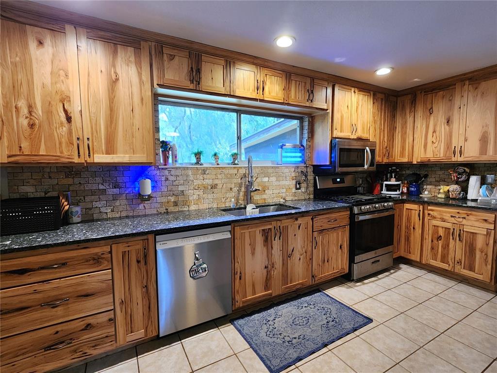 A kitchen features rustic wood cabinets, dark granite countertops, and a tiled backsplash — 13501 NE 245TH STREET ROAD, FORT MC COY, FL