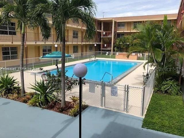 A swimming pool sits in the courtyard of a multi-story apartment building with palm trees — 3881 W FLAGLER STREET UNIT 102, MIAMI, FL