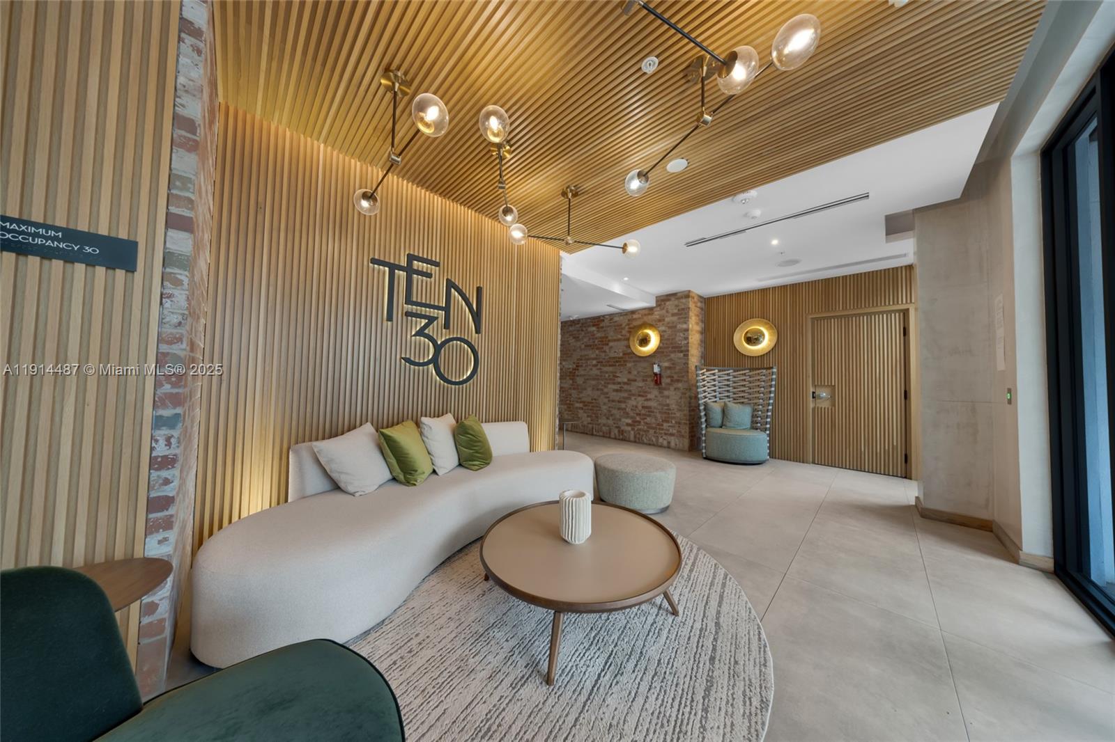 A modern lobby features a curved sofa, wood-slatted walls, and a circular coffee table — 1030 15th St # 306, Miami Beach FL 33139, MIAMI BEACH, FL