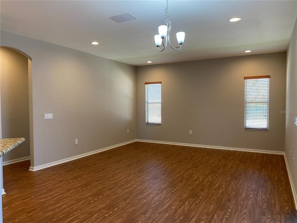 An empty room features wood-look flooring, light gray walls, a chandelier, and two windows — 481 PHEASANT DRIVE, HAINES CITY, FL