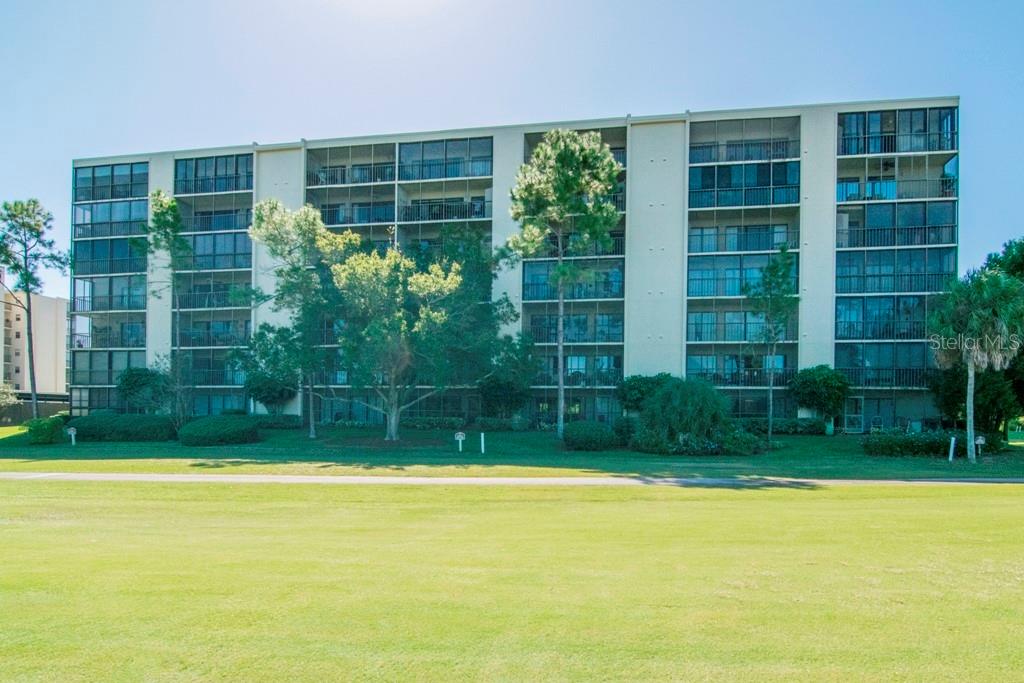 A multi-story apartment building with screened balconies overlooks a grassy lawn — 3300 COVE CAY DRIVE UNIT 1C, CLEARWATER, FL