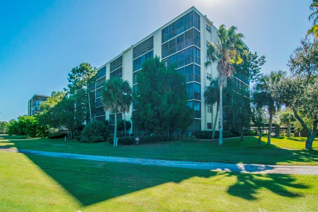A multi-story residential building with screened balconies stands on a grassy lawn with palm trees — 3300 COVE CAY DRIVE UNIT 1C, CLEARWATER, FL