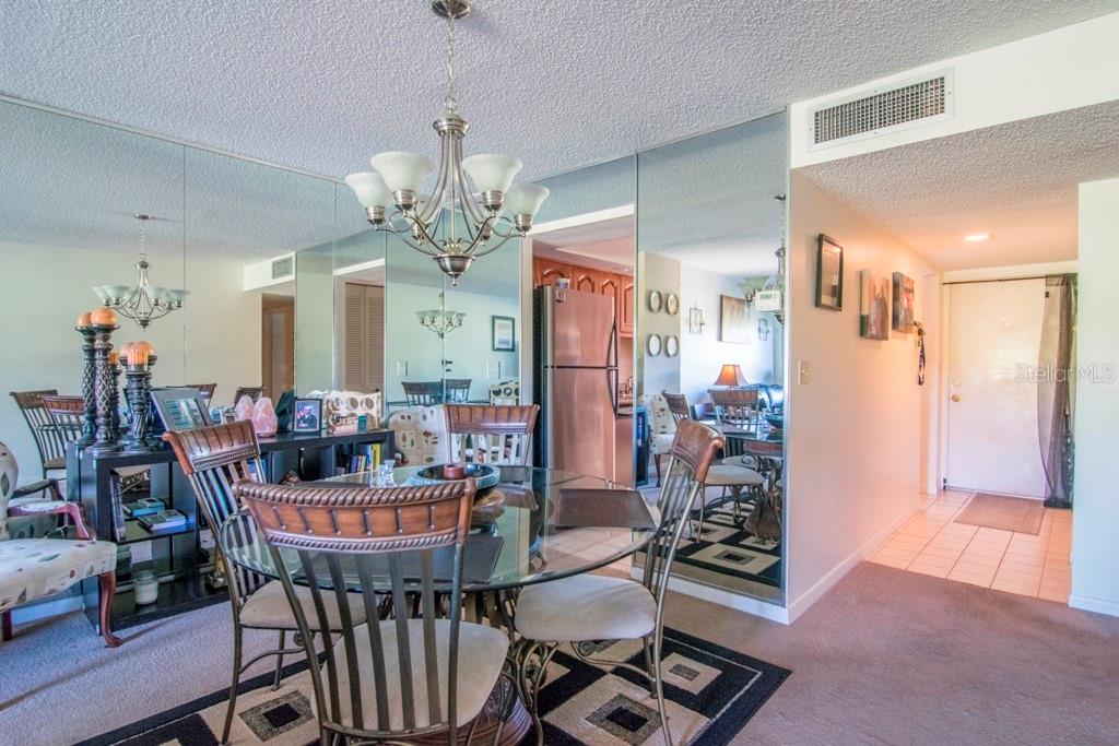 A dining area features a glass table, mirrored walls, and a chandelier on carpeted flooring — 3300 COVE CAY DRIVE UNIT 1C, CLEARWATER, FL