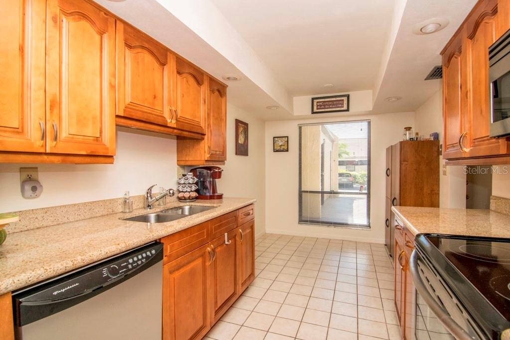 A kitchen features wood cabinets, granite countertops, a stainless steel dishwasher, and a windowed wall — 3300 COVE CAY DRIVE UNIT 1C, CLEARWATER, FL