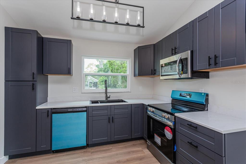 A kitchen features dark gray cabinets, white countertops, stainless steel appliances, and wood-look flooring — 7728 BALHARBOUR DRIVE, NEW PORT RICHEY, FL