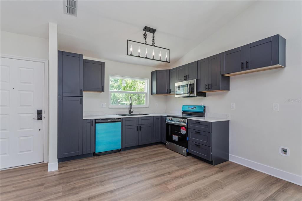 A kitchen features dark gray cabinets, stainless steel appliances, and wood-look flooring — 7728 BALHARBOUR DRIVE, NEW PORT RICHEY, FL
