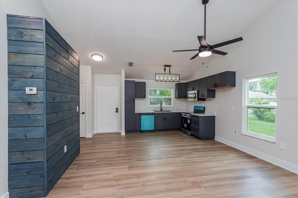 A kitchen and living area featuring dark blue cabinets, wood-look flooring, and a shiplap accent wall — 7728 BALHARBOUR DRIVE, NEW PORT RICHEY, FL