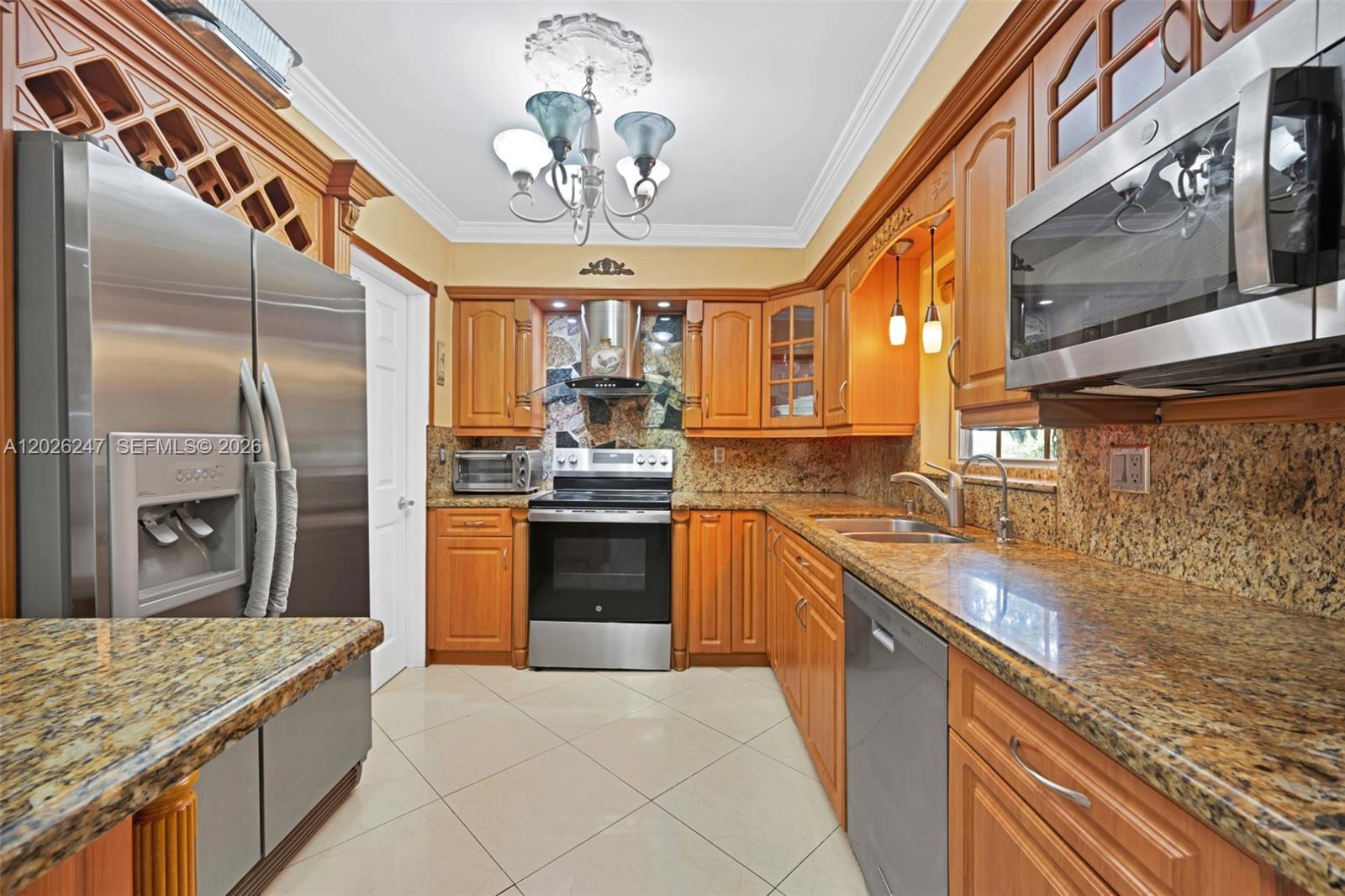 A kitchen features wood cabinets, granite countertops, stainless steel appliances, and a chandelier — 2849 Dewey St # 2849, Hollywood FL 33020, HOLLYWOOD, FL