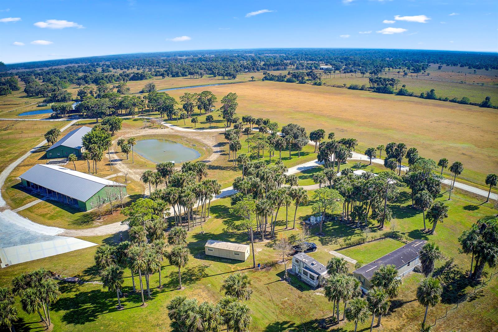 An aerial view shows a rural property with two large barns, a pond, and outbuildings — 30003 SW Martin Highway, Okeechobee FL 34974, OKEECHOBEE, FL