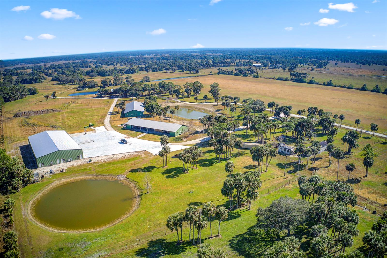An aerial view shows a large rural property with multiple metal buildings, ponds, and palm trees — 30003 SW Martin Highway, Okeechobee FL 34974, OKEECHOBEE, FL