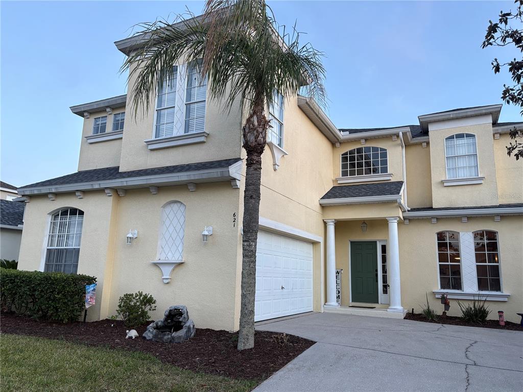 A two-story yellow stucco house features a palm tree, a garage, and a front entrance — 621 COPELAND DRIVE, HAINES CITY, FL