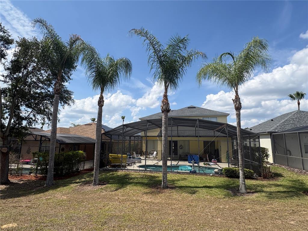 A backyard features a swimming pool enclosed by a screen cage and three tall palm trees — 621 COPELAND DRIVE, HAINES CITY, FL
