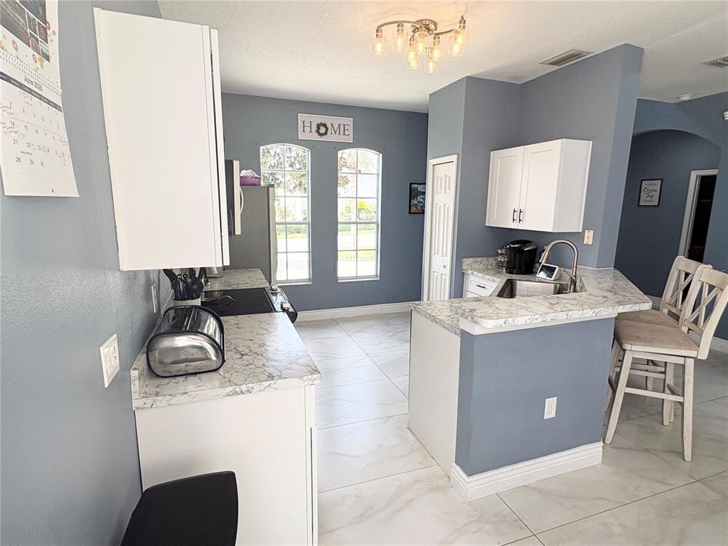 A kitchen features blue walls, white cabinets, marble-look countertops, and a breakfast bar with stools — 621 COPELAND DRIVE, HAINES CITY, FL