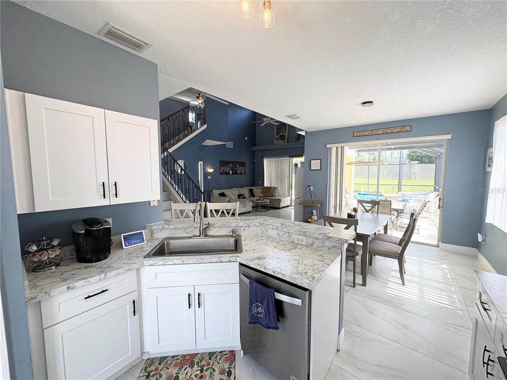 A kitchen with white cabinets and marble-look countertops overlooks a dining area and living room — 621 COPELAND DRIVE, HAINES CITY, FL