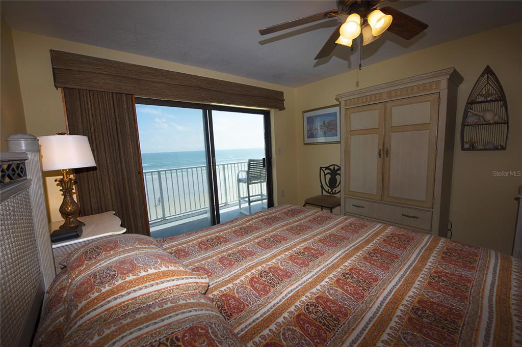 A bedroom features a patterned bedspread, a wooden armoire, and a sliding door to a balcony — 1571 S ATLANTIC AVENUE UNIT 309, NEW SMYRNA BEACH, FL