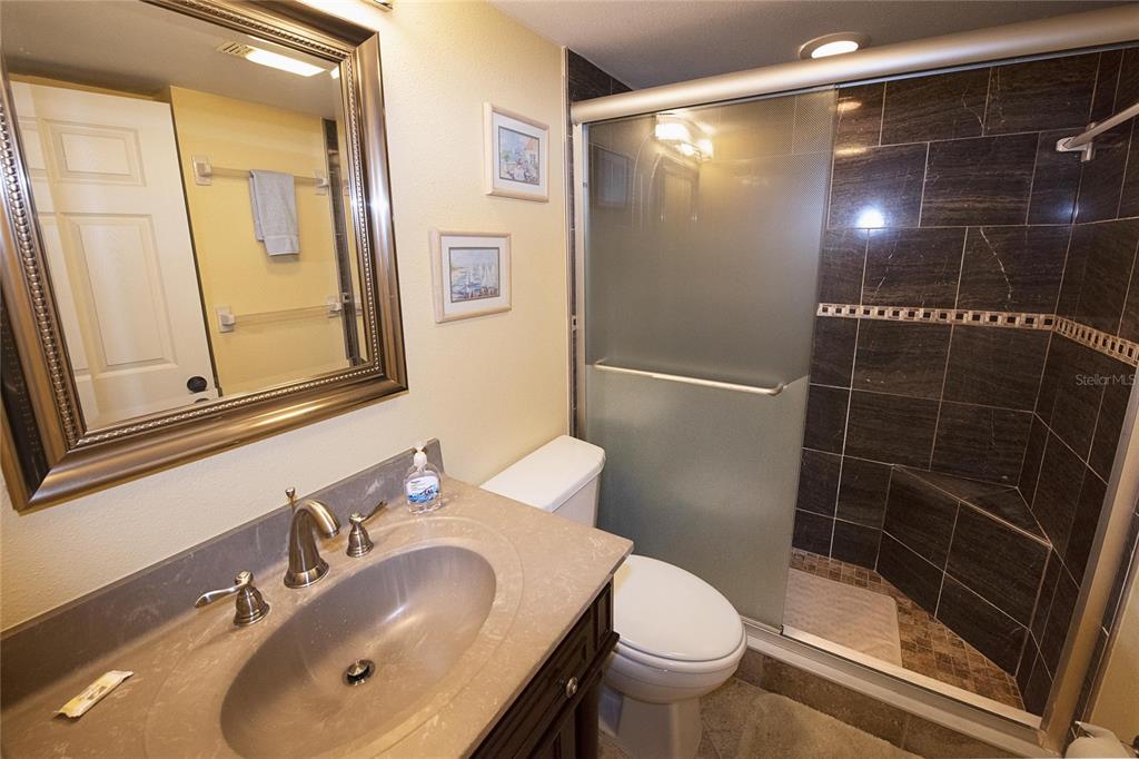 A bathroom features a vanity with a stone countertop, a toilet, and a tiled shower — 1571 S ATLANTIC AVENUE UNIT 309, NEW SMYRNA BEACH, FL