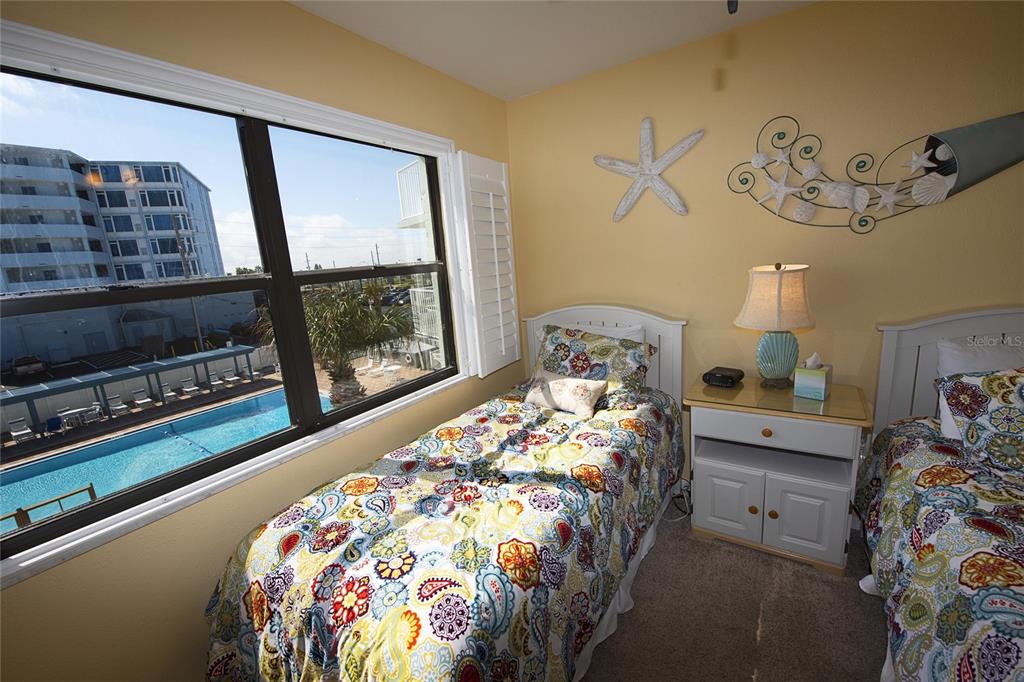 A bedroom with two twin beds, a nightstand, and a window overlooking a swimming pool — 1571 S ATLANTIC AVENUE UNIT 309, NEW SMYRNA BEACH, FL