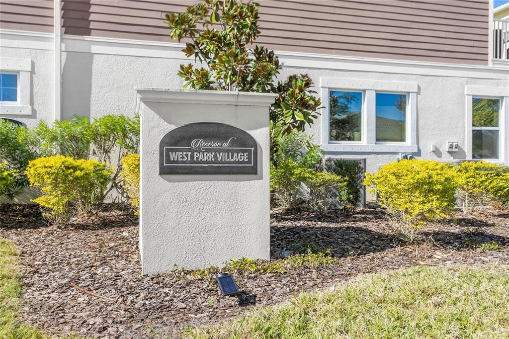 A white stucco monument sign for Reserve at West Park Village sits in a garden — 9597 CAVENDISH DRIVE, TAMPA, FL