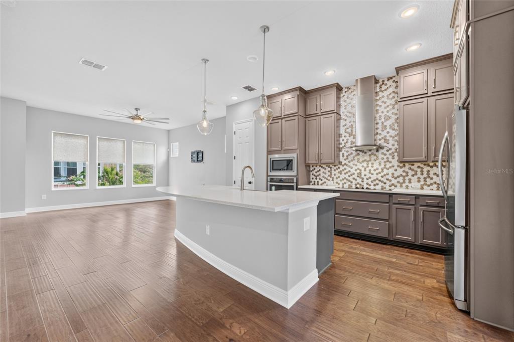 A kitchen with grey cabinets, a white island, and a patterned backsplash opens to a living area — 9597 CAVENDISH DRIVE, TAMPA, FL