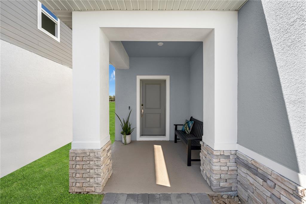 A covered front porch features stone-based columns, a gray door, and a black wooden bench — 3812 SENNA WAY, TAVARES, FL
