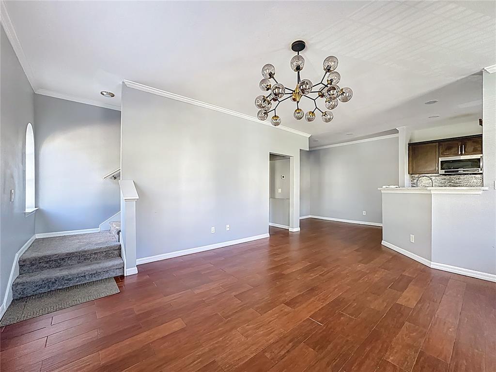 An open living area features hardwood floors, gray walls, a modern chandelier, and carpeted stairs — 760 SIENA PALM DRIVE UNIT 205, KISSIMMEE, FL