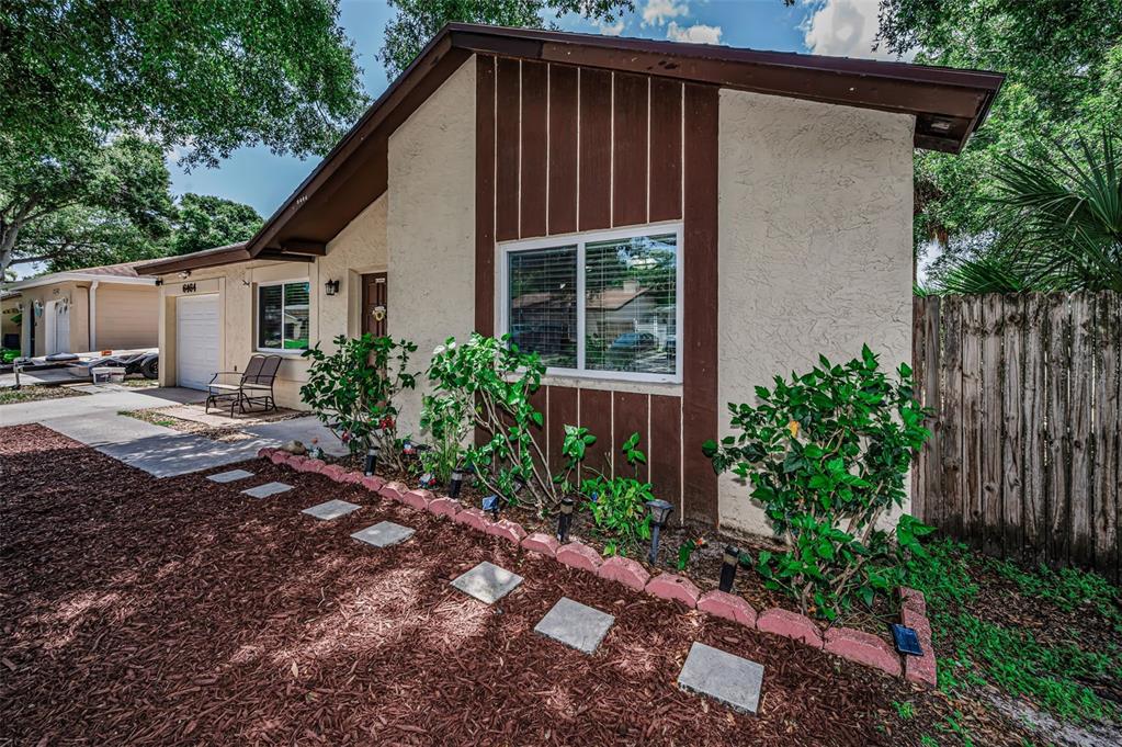 A single-story house exterior features a brown and beige facade with a front garden bed — 6464 107TH TERRACE N, PINELLAS PARK, FL