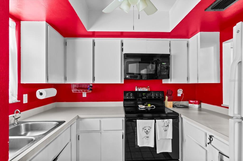 A kitchen features white cabinets, a black stove and microwave, and bright red walls — 1219 MACKERAL AVENUE, SARASOTA, FL