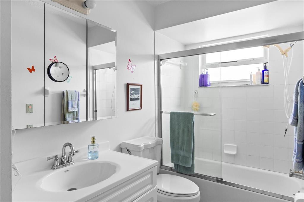 A bathroom features a white vanity, a medicine cabinet, a toilet, and a shower-tub combo — 1219 MACKERAL AVENUE, SARASOTA, FL