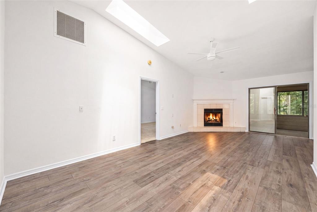 A living room with wood-look flooring, a fireplace, a ceiling fan, and a skylight — 2401 NW 69TH TERRACE, GAINESVILLE, FL