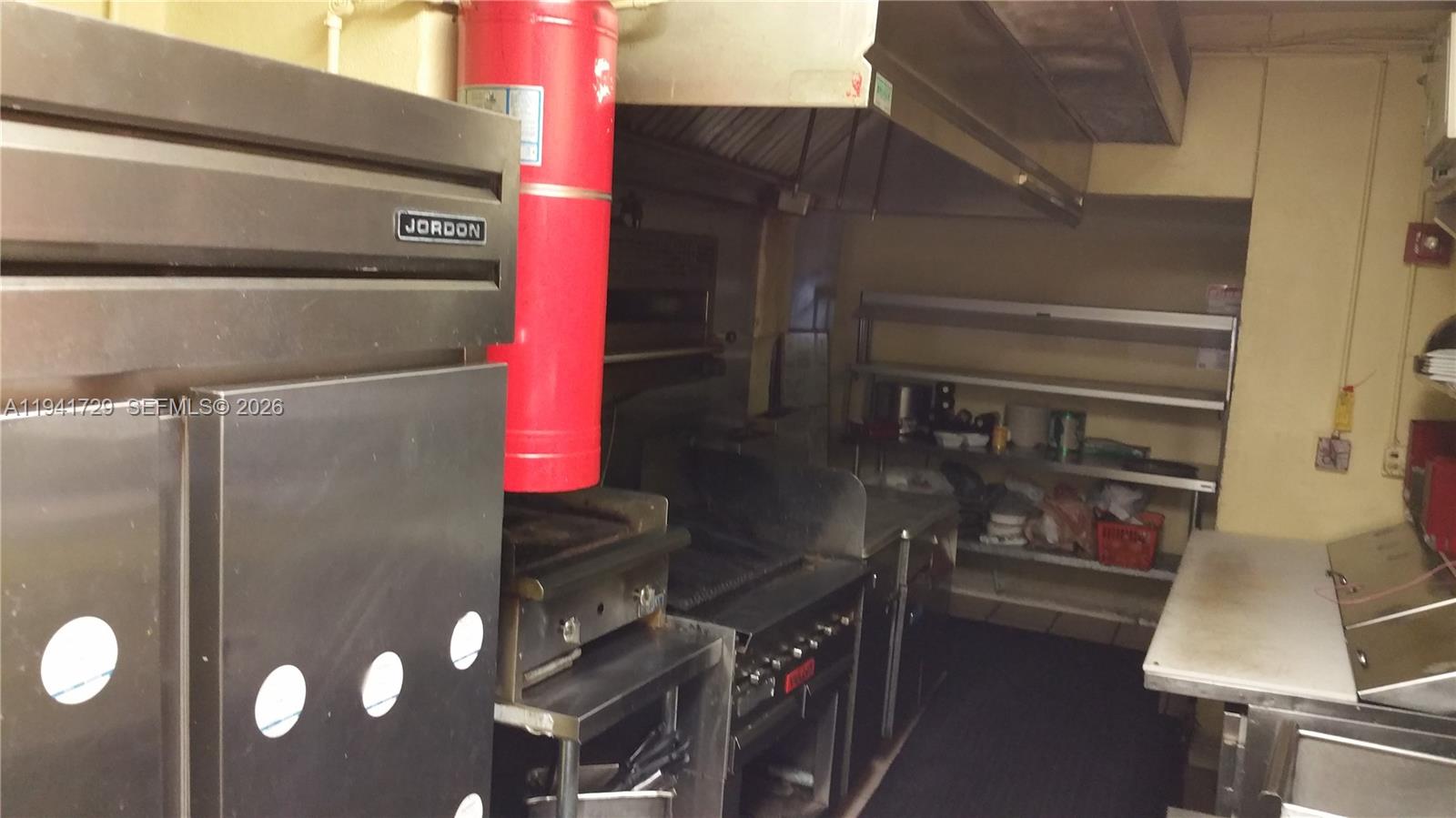 A commercial kitchen features stainless steel appliances, a red fire extinguisher, and metal shelving units — 13914 NW 7th Ave, Miami FL 33168, MIAMI, FL
