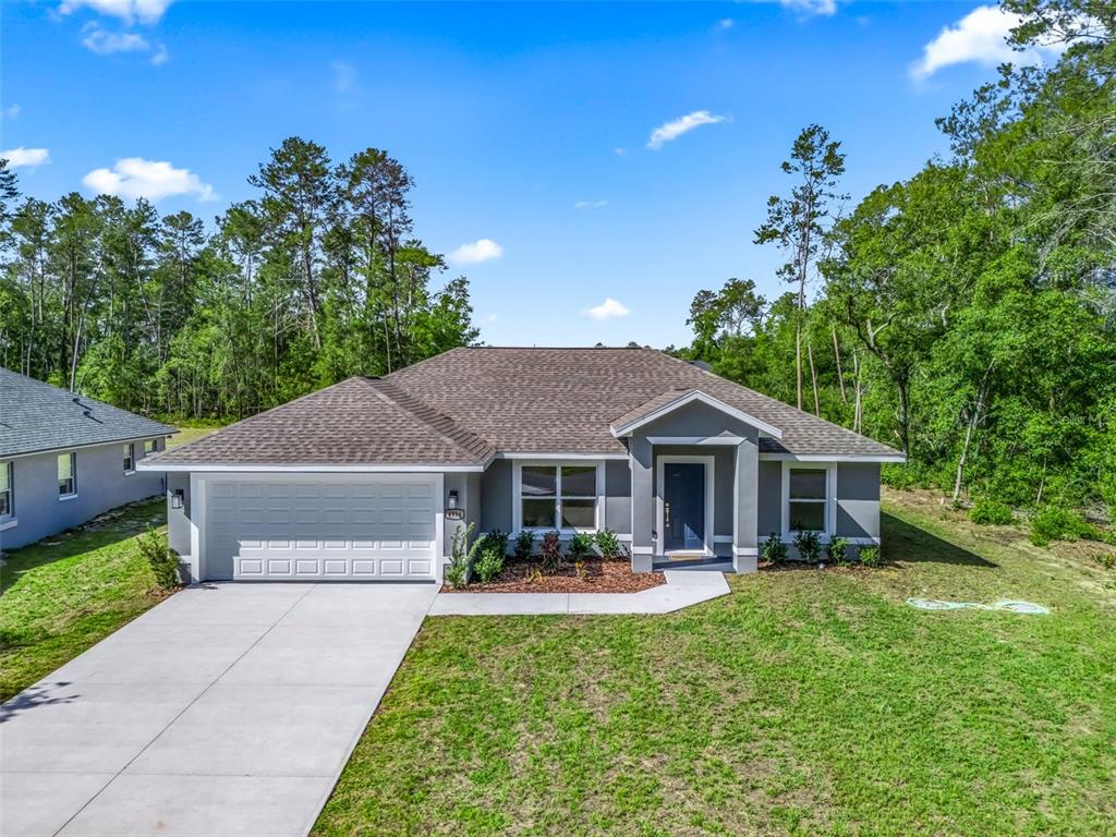 A single-story gray house with a two-car garage sits on a grassy lot near trees — 4994 SW 166TH LOOP, OCALA, FL