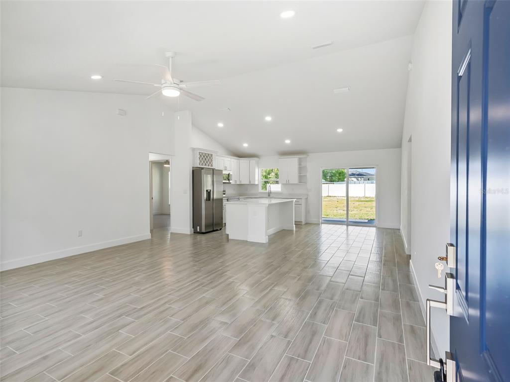 An open-concept kitchen and living area with light wood-look tile flooring and white cabinetry — 4994 SW 166TH LOOP, OCALA, FL